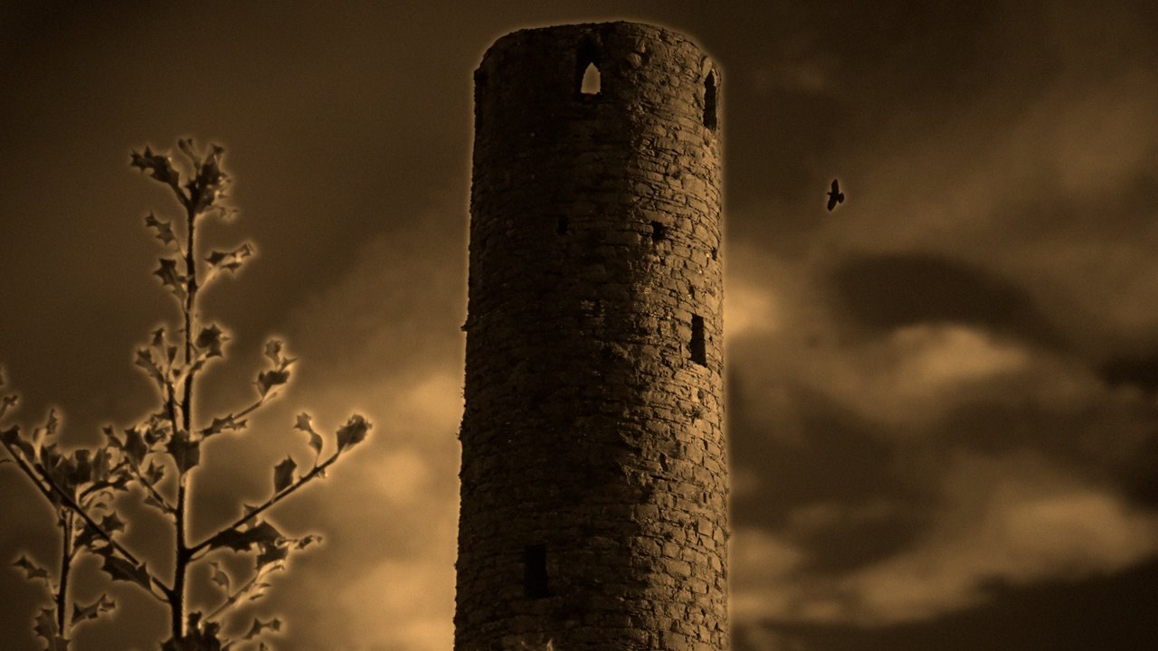 The Kells Round Tower, its conical cap long gone, in warm evening light — flat open top against a cloudy sky