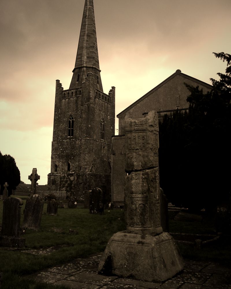 A broken high cross in the churchyard at Kells, with St Columba’s Church and its spire behind