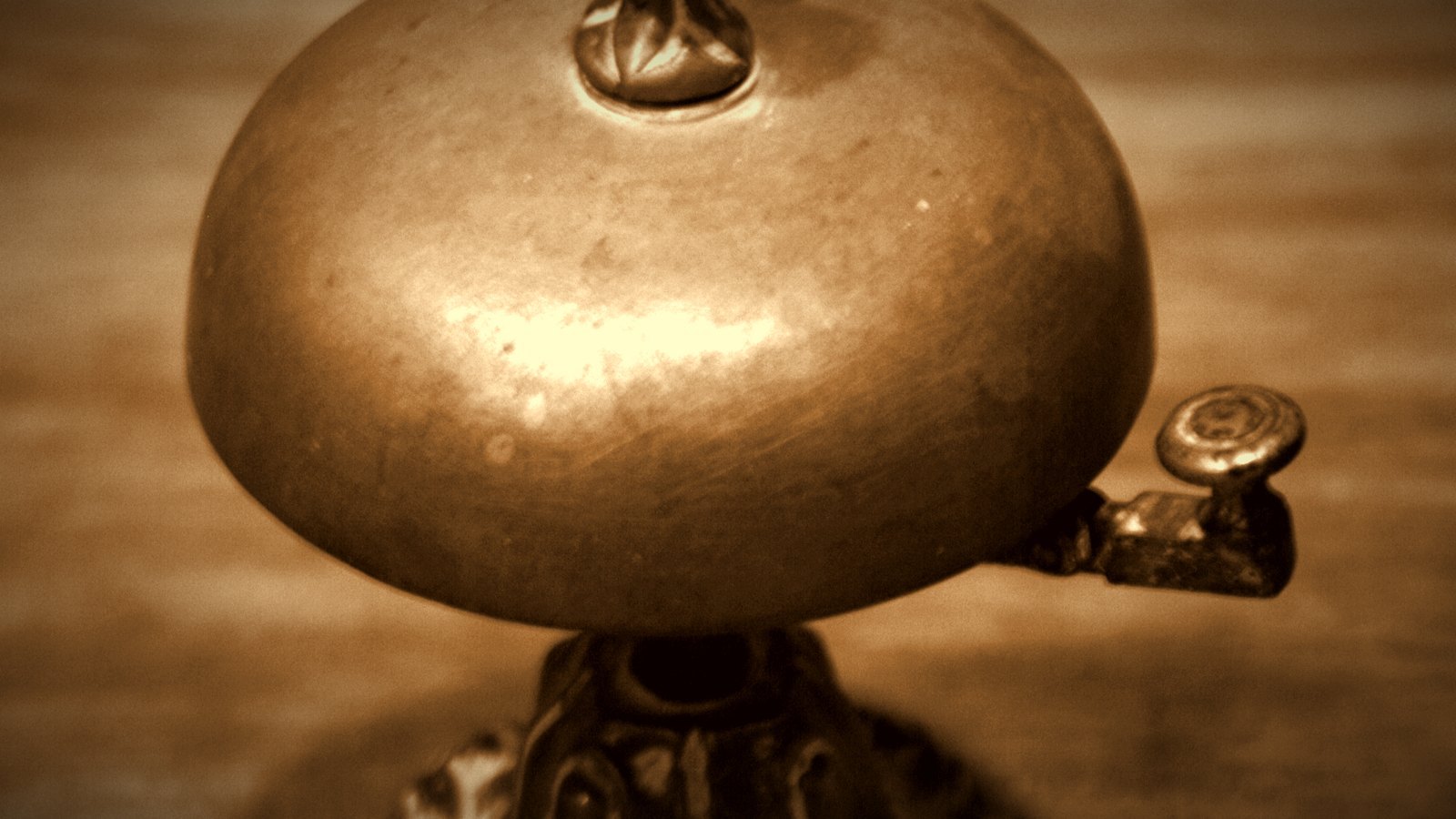 Close-up of a brass counter service bell on a wooden surface; warm sepia tones