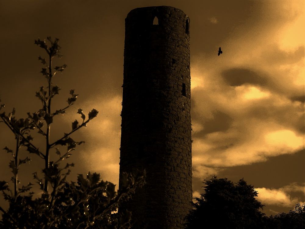 The uncapped Round Tower of Kells rising above trees against a stormy sky